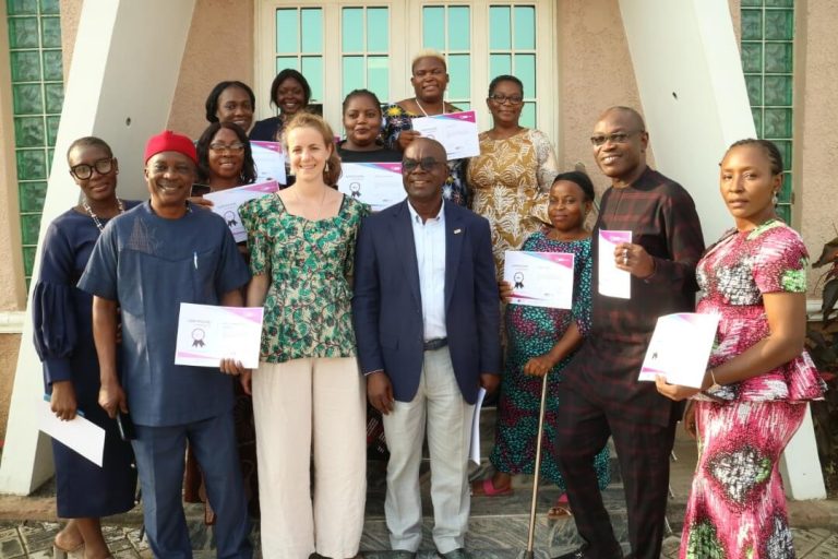 Trainees holding certificate with trainer Nadege in front of the training building