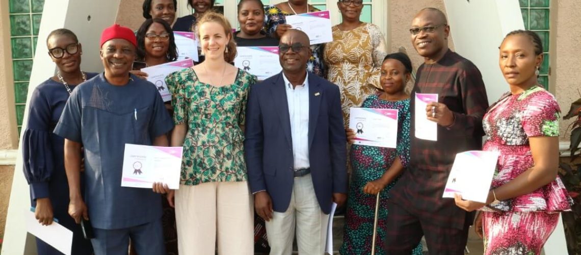 Trainees holding certificate with trainer Nadege in front of the training building